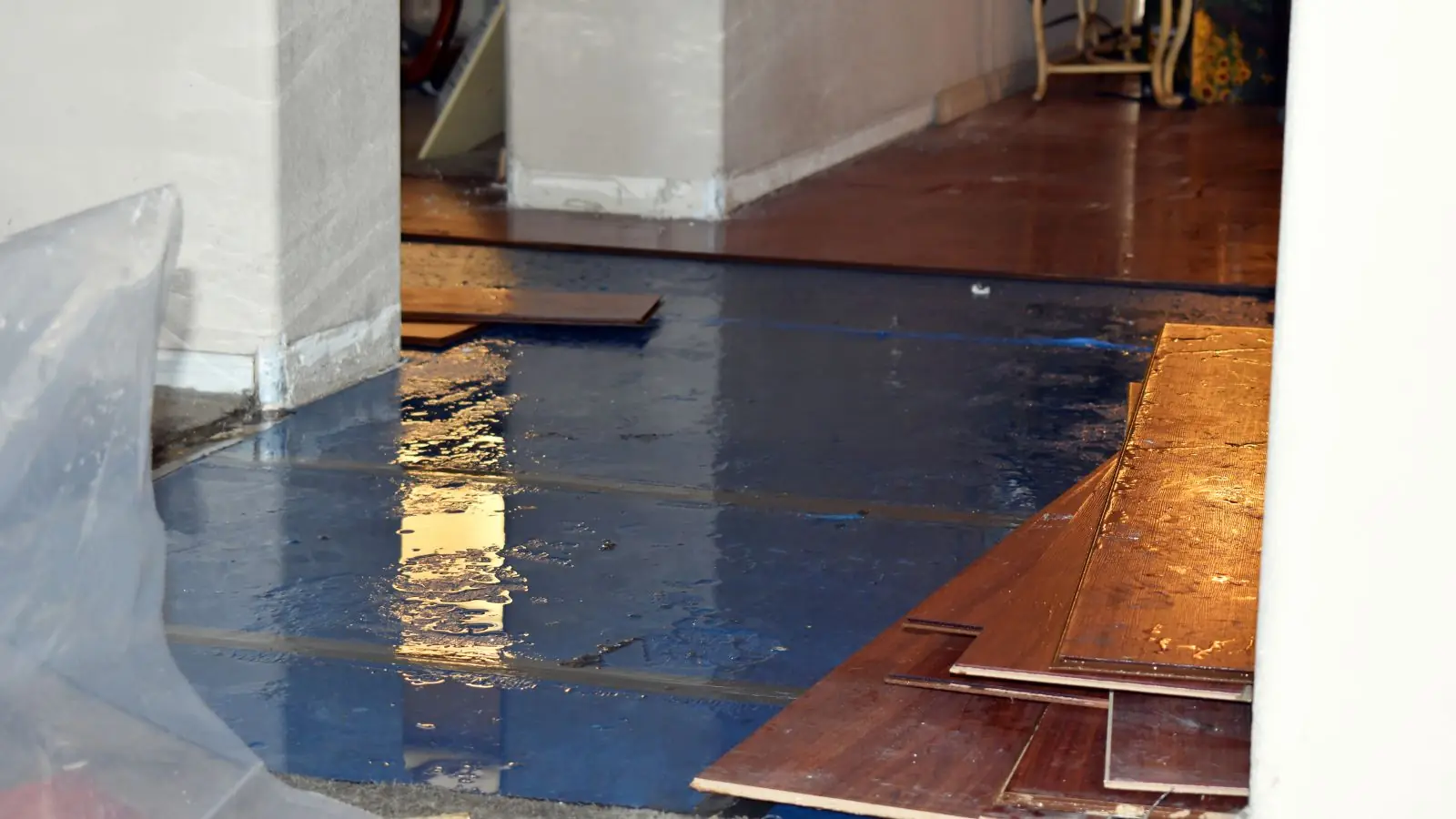 Hardwood boards lifted from a wet floor covered in protective plastic